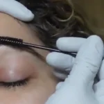 Brow lamination course preview: gloved hands brushing laminated brows upward with a spoolie